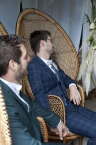 Deux mariés élégants assis côte à côte dans des fauteuils emmanuelle en rotin lors de leur cérémonie laïque au Domaine de la Hétraie