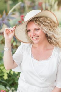 Portrait souriant de Laëtitia, officiante de cérémonie laïque, tenant un chapeau de paille en extérieur
